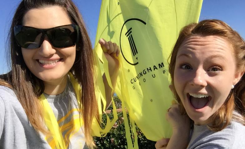 Two women taking a break from flying a kite to excitedly smiling at the camera